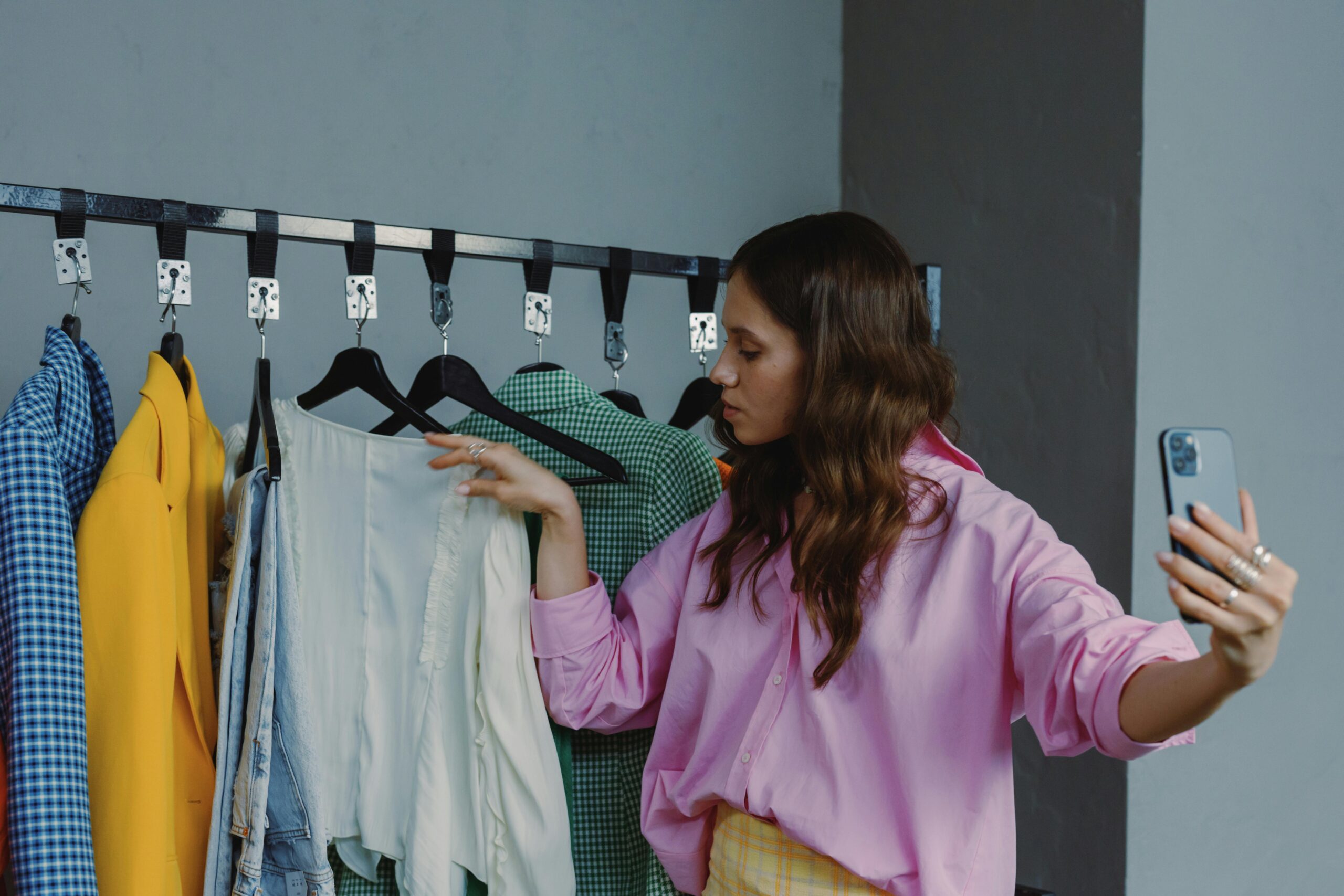 A woman selects clothes to create an outfit while taking a selfie, showcasing fashion choices.